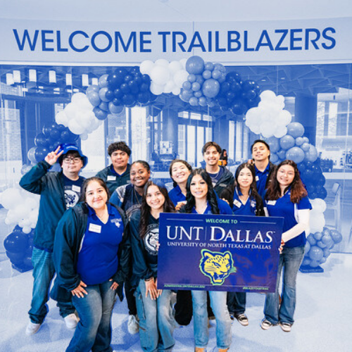 A group of students posing and smiling while holding a UNT Dallas yardsign.