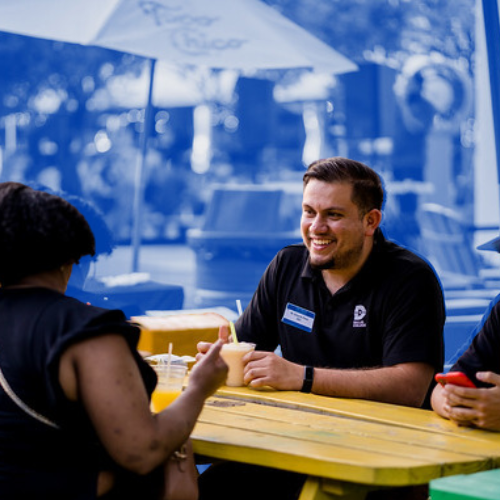 Alumni sitting at a picnic table, talking, and smiling. 