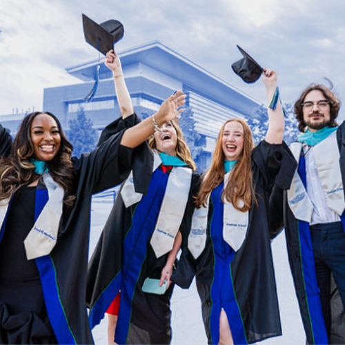 Four graduates dressed in regalia, throwing their caps in the air, and smiling at the camera.