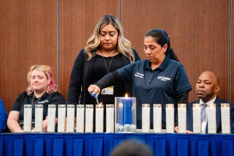 Maria Lopez, a Member of the Facilities Team, Lights a Candle in Memory of Her Husband, Isidro Lopez Catalan, Who Was Also an Employee, as Amanda Reyes, Sr. Executive Asst., Stands in Support