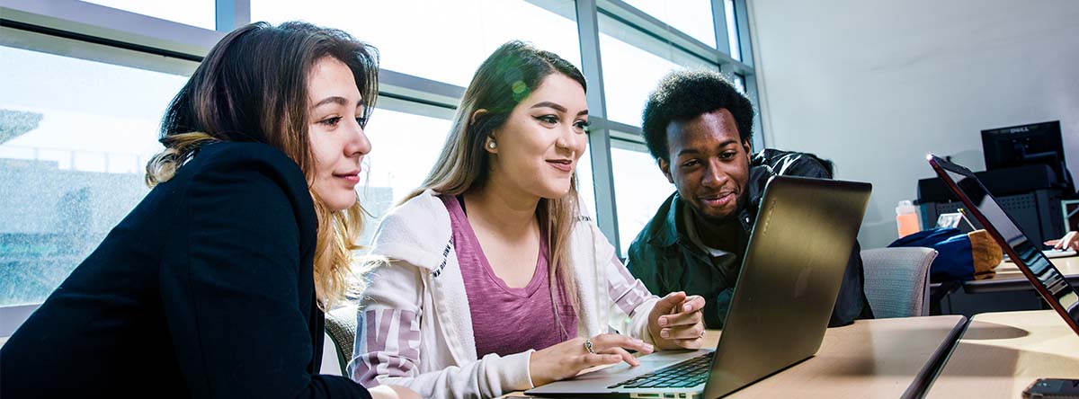 
three students in class sharing laptop
