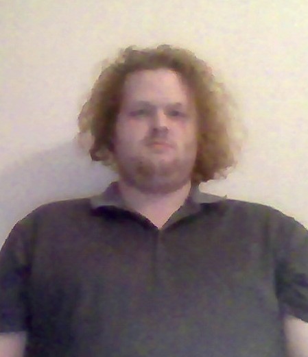 man with curly hair in a dark shirt against a white wall