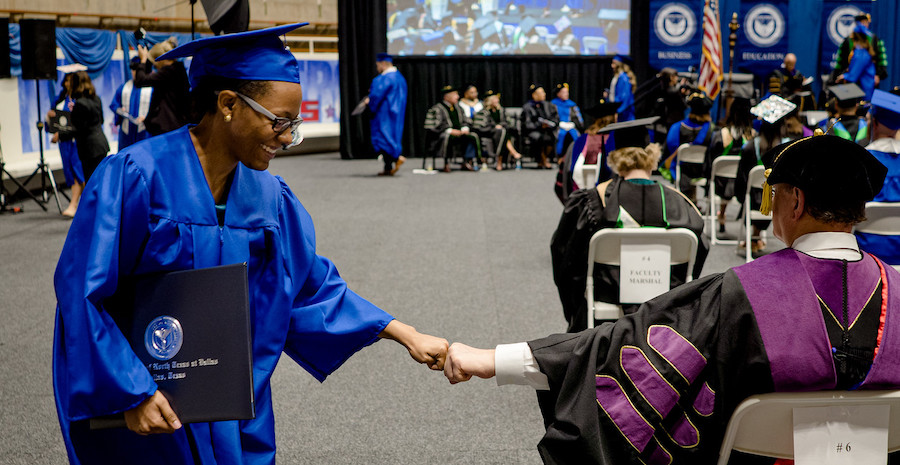 graduate bumping fist with faculty
