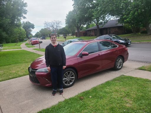 young man in black hoodie standing in front of red car