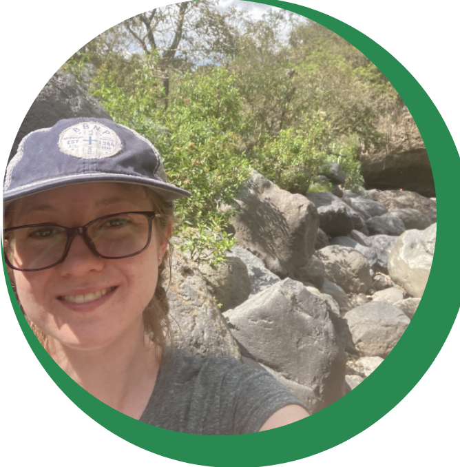 smiling woman in nature wearing a gray hat, gray shirt, and black glasses