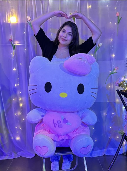 woman smiling with arms in a heart shape standing behind a large, plush hello kitty