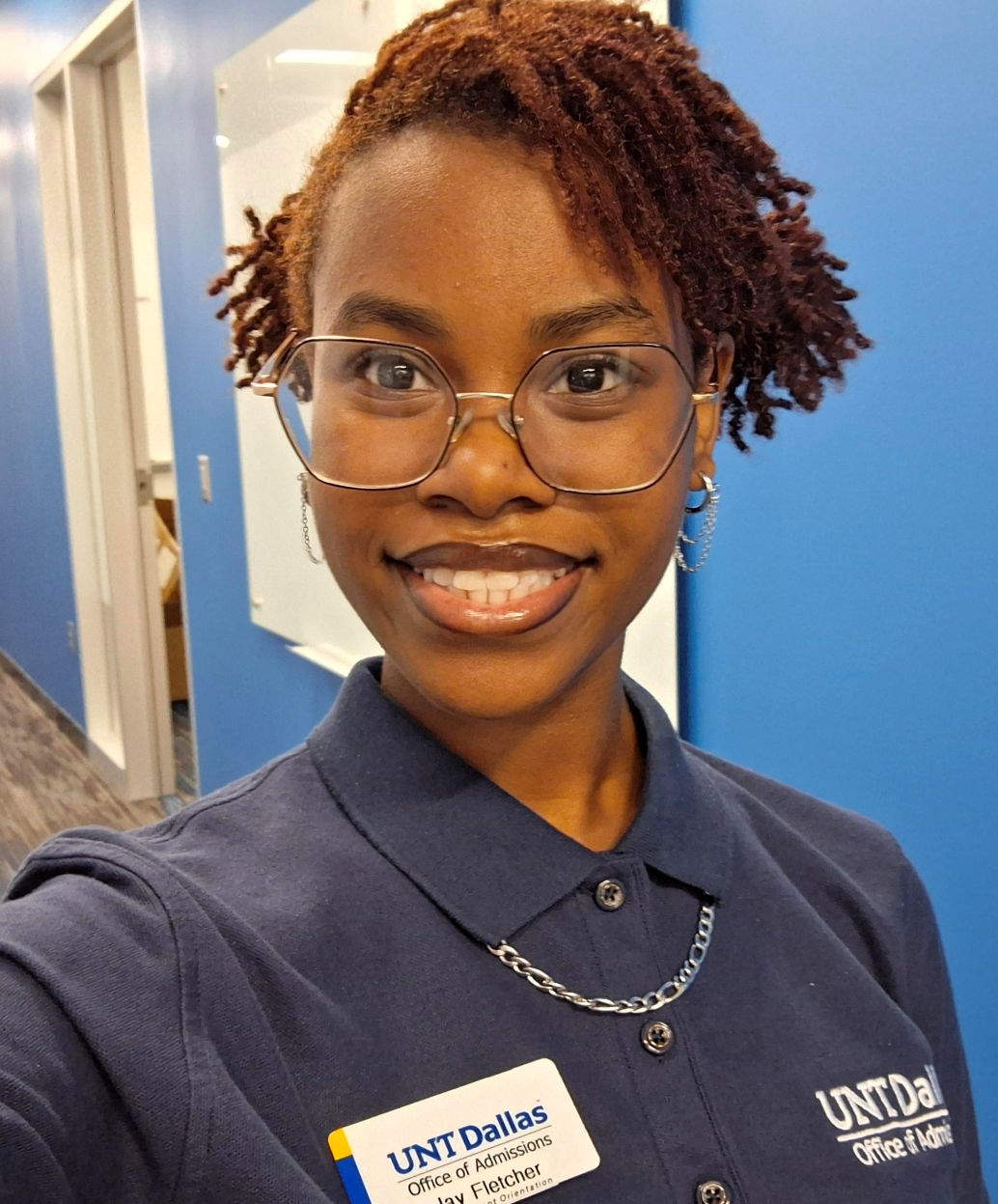 black woman smiling in glasses wearing a collared, royal blue shirt