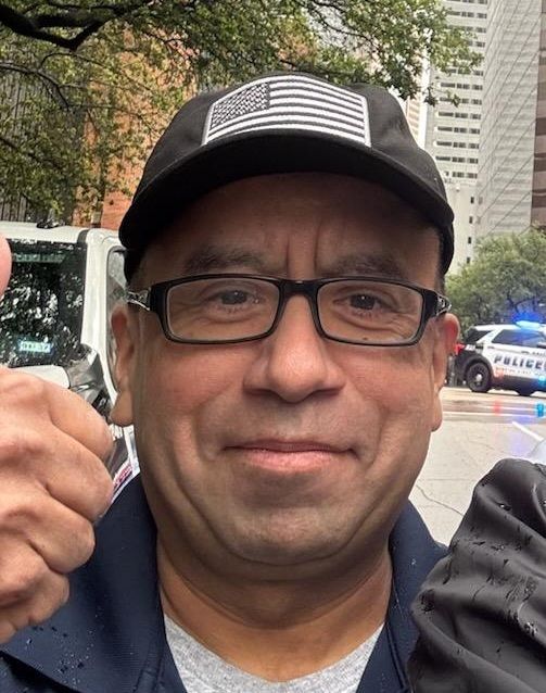 man smiling with a thumbs in a black cap in a downtown neighborhood