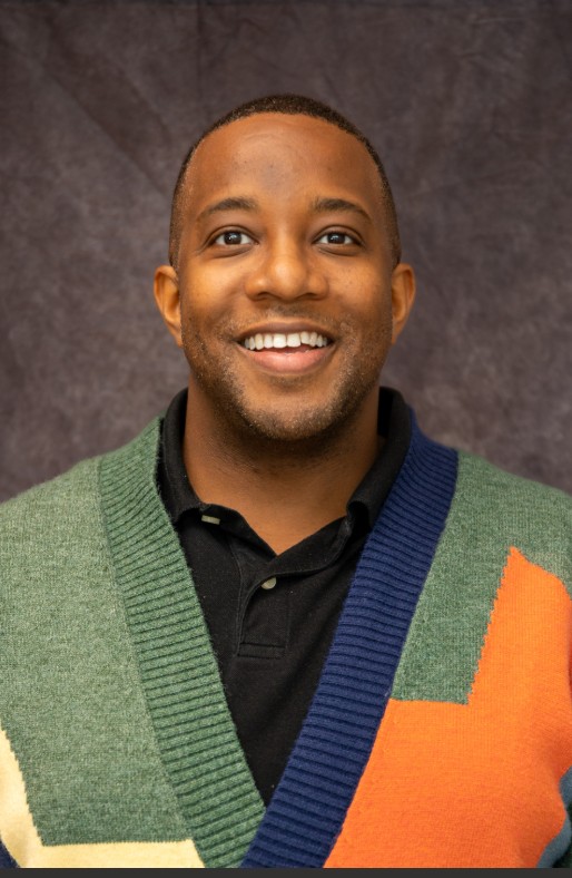 black male in multicolor sweater and black polo smiling