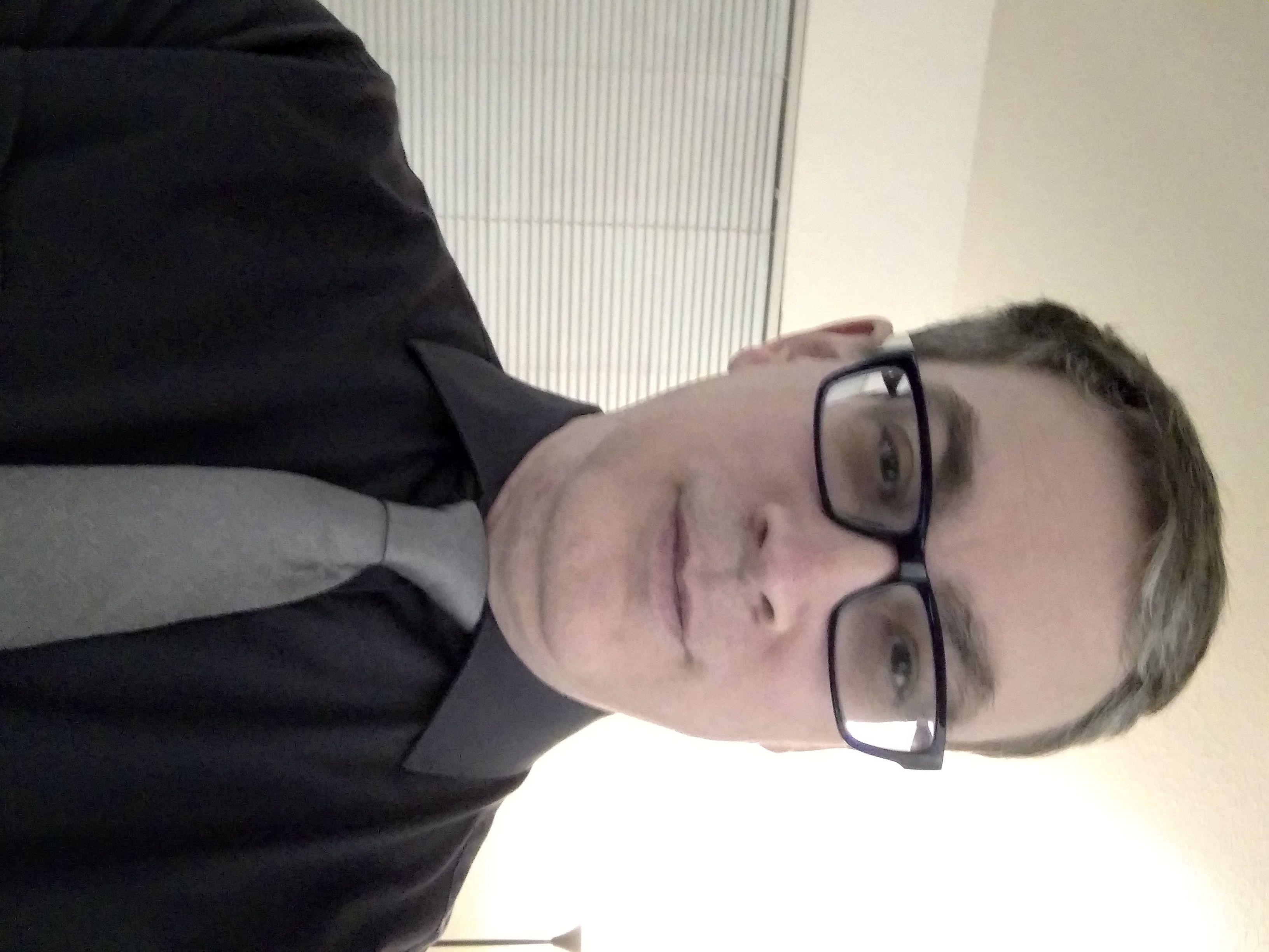 man in dark glasses, black shirt, and gray tie